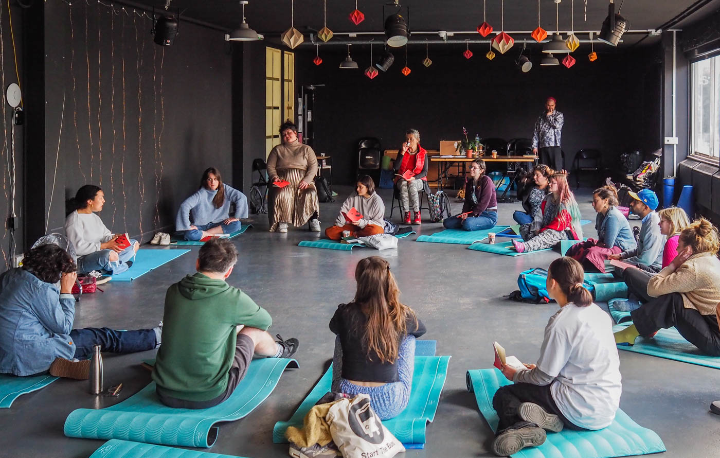 A group of adults sitting on the floor on yoga mats in a studio setting