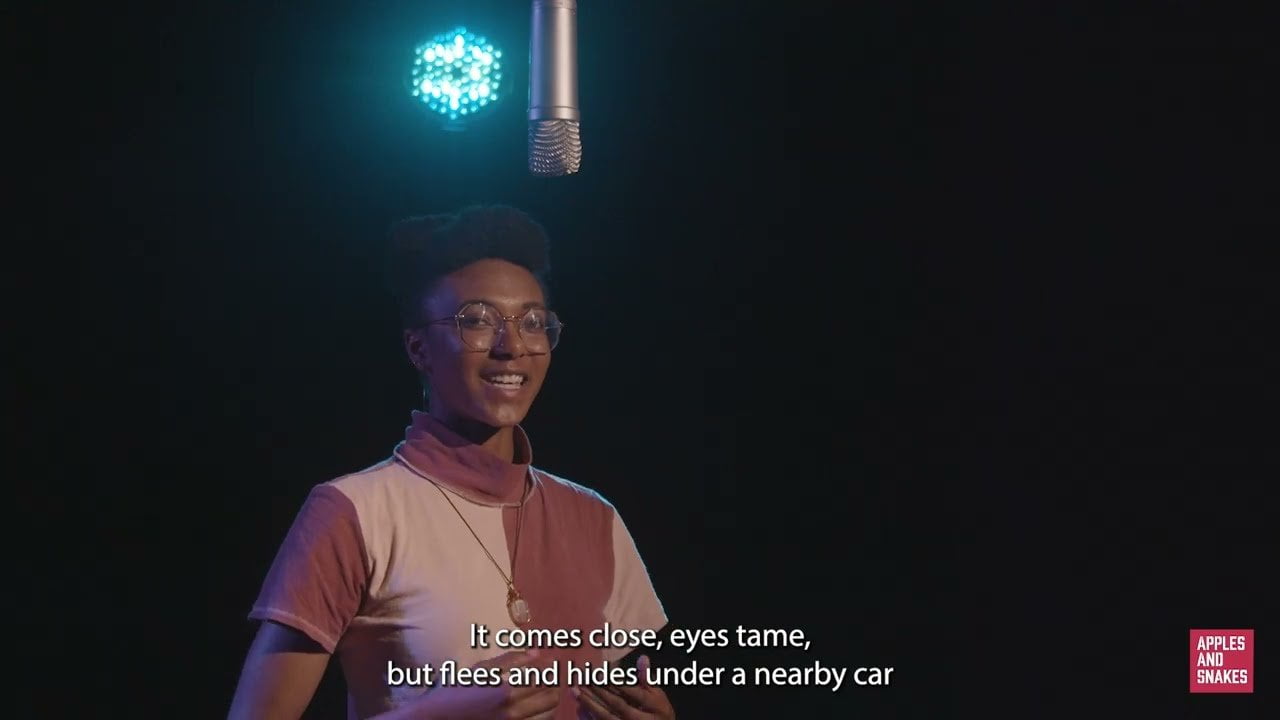 Screenshot from a video of Ingrid speaking into a microphone in a dark room with a blue light