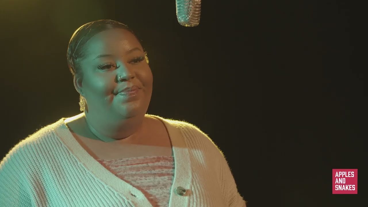 Imagine of Lashay speaking into a microphone in a dark room with pale green lighting