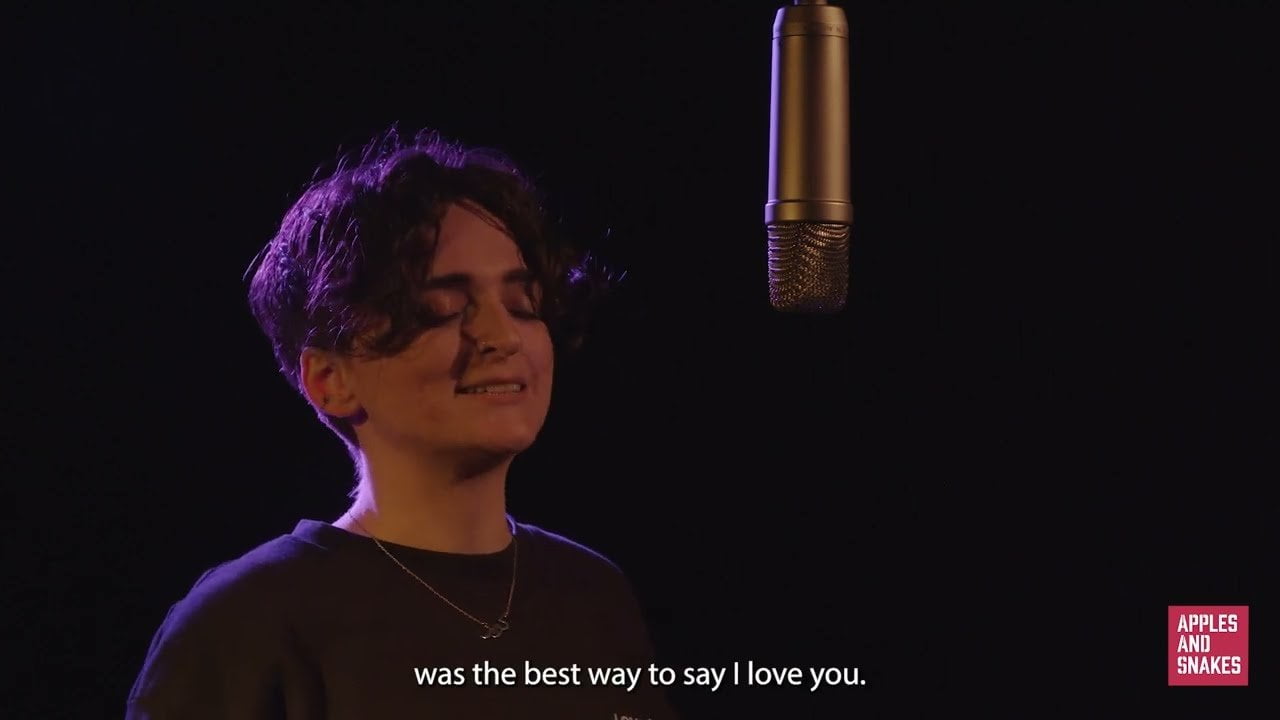 Screenshot from a video of Lisa speaking into a microphone in a dark room with purple lighting