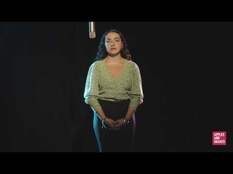 Screenshot from a video of Rojbin speaking in to a microphone in a dark room