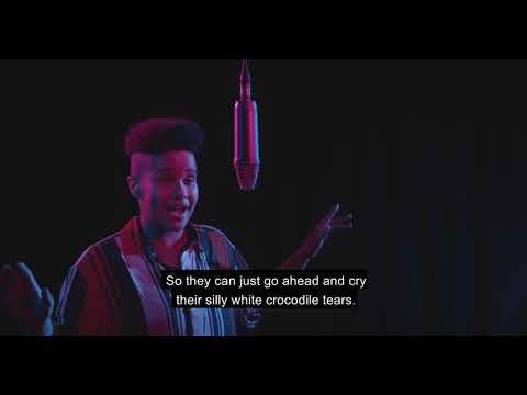 Screenshot of a video of Subria speaking into a microphone in a dark room with pink lighting