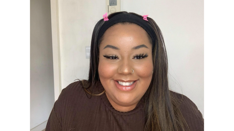 A woman with pink clips in her hair and wearing brown top, smiles