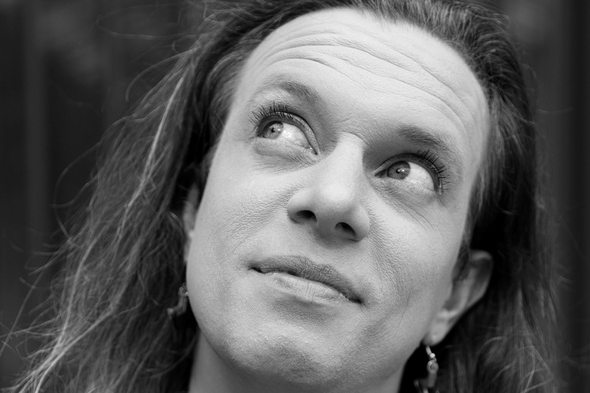 Edalia looks to the side and up, wearing her hair down, with hoop earrings.