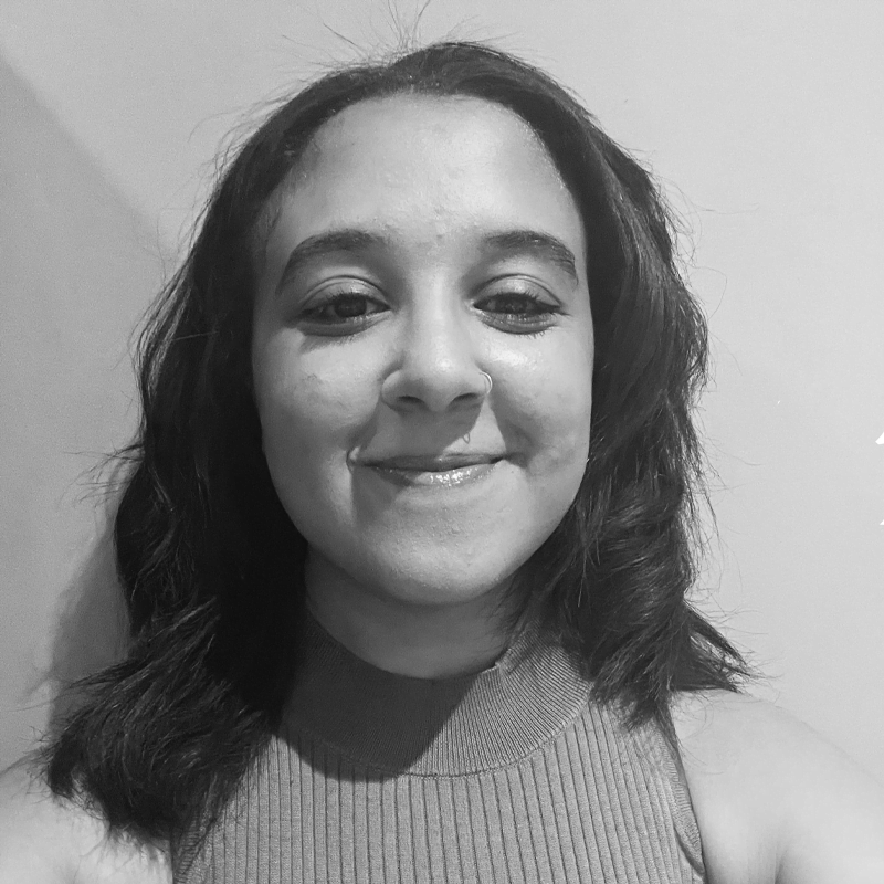 a woman with wavy, thick dark hair that is centre parted, smiling.