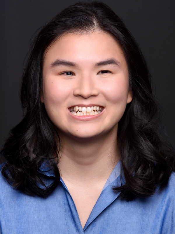 Jasmin has mid length brown hair, smiling, wearing an open blue shirt