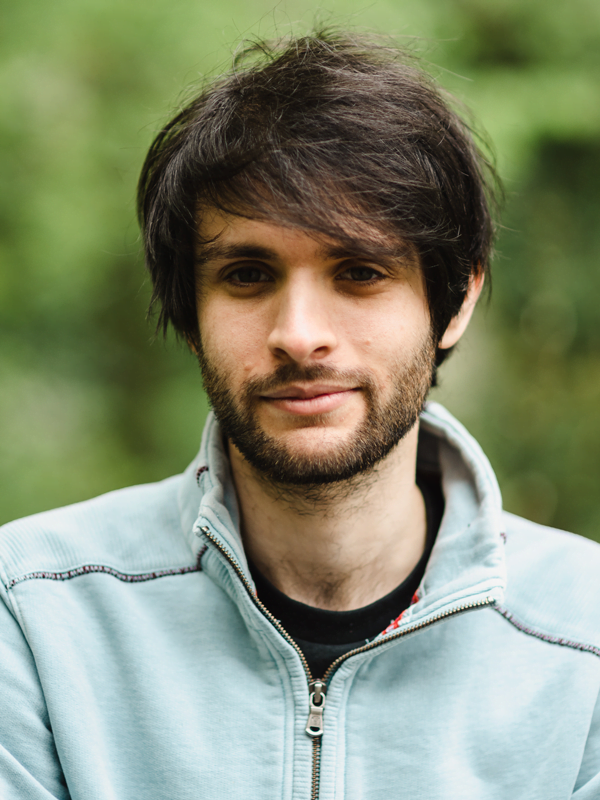 Jonah has dark hair, swept to the side. Wearing a light blue zip up hoody