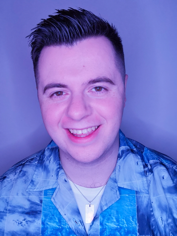 Kane has short, gelled spiked hair. Wearing a blue square patterned shirt