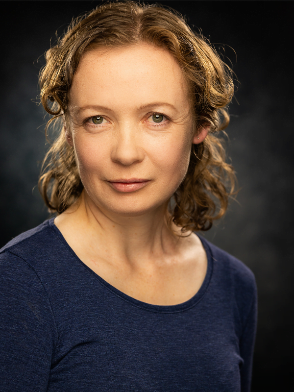 Lesley wears her light brown wavy hair in a half up style with a dark blue long sleeve top