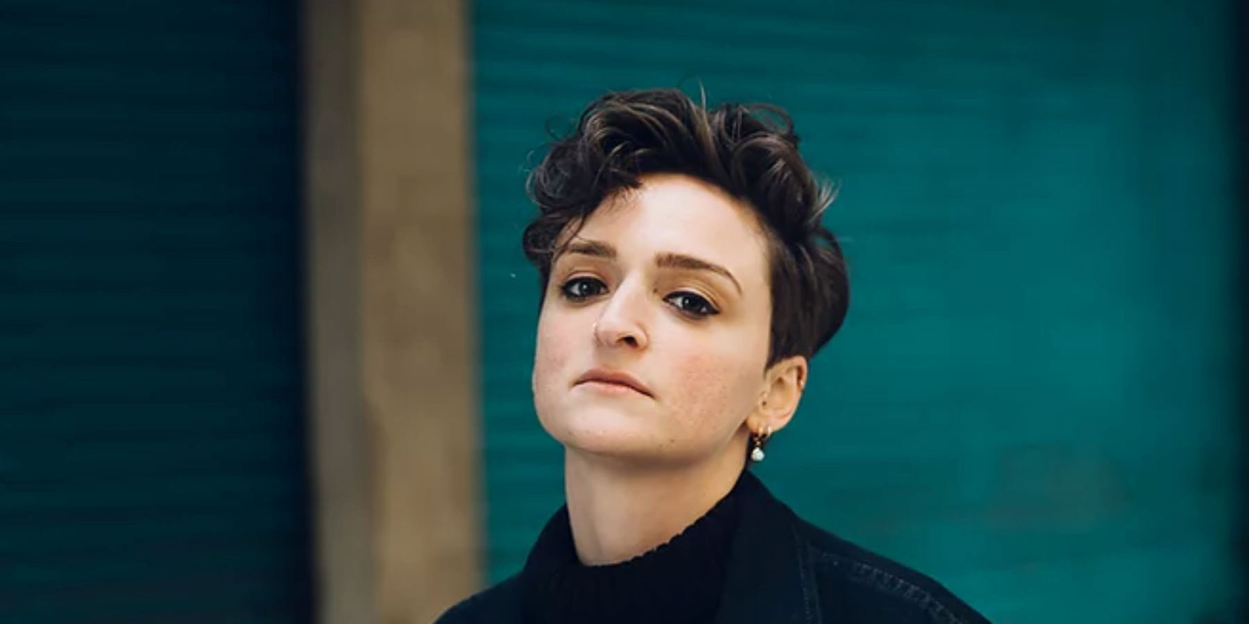 a woman with short cropped hair and pear earring tilts her head towards the camera
