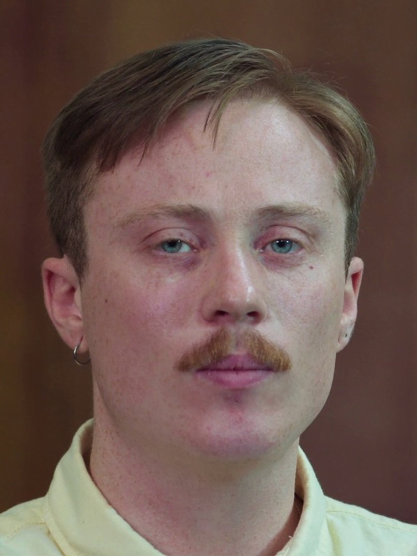 Matt has short, side parted brown/red hair and ginger moustache. Wearing a hoop earring on the left side and yellow collared shirt