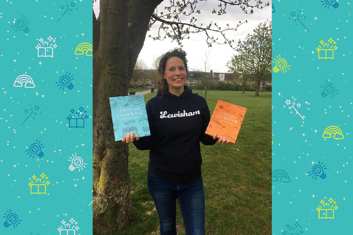 An image of artist Nancy Ellis, she stand in a green park next to aa tree an holds an orange book and a blue book. She wears a blue hoodie with some white writing on the form and blu jeans. She has shoulder length hair and smiles at the camera.