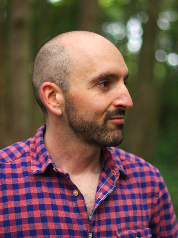 Polis looks sideway on, short shaved head and beard, in a red and blue tartan shirt