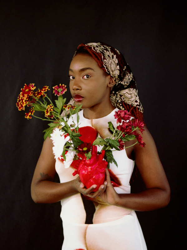 Princess wears a flower headscarf in black, red and white. Holding a red heart vase with yellow and red carnations.