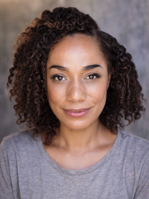 Tanya has bob length curly dark hair, wearing a grey tshirt looking neutral