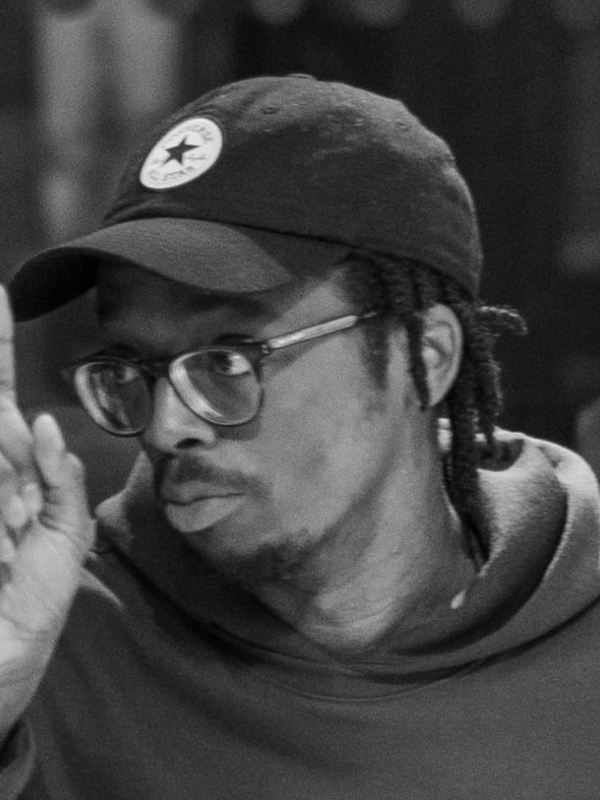 Toreh wears a converse cap, glasses. hoody and looks engaged.